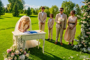 Булката подписва брачния акт, докато младоженецът и синовете им я наблюдават с гордост по време на изнесен ритуал в Голф клуб "Св. София". Кадър от сватбен фотограф Симеон Сълов.