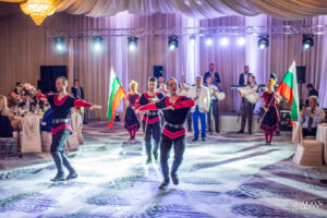 Професионални танцьори в народни носии изпълняват динамичен български танц като част от фолклорната програма на сватбата в хотел Маринела, кадър на професионален сватбен фотограф Симеон Сълов.