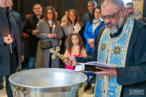 Свещеникът благославя водата в купела с кръст в ръка, преди потапянето на малкия Борис по време на неговото кръщение. Кадър от професионален фотограф за кръщене Симеон Сълов.