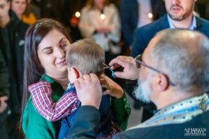 Свещеникът символично подстригва косата на малкия Борис, докато майка му го гледа с нежна усмивка. Кадър от професионален фотограф за кръщене Симеон Сълов.