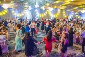 Голямата бална зала на хотел "Маринела" е изпълнена със стотици гости, танцуващи българско хоро по време на пищно сватбено тържество. Кадър от сватбен фотограф Симеон Сълов.