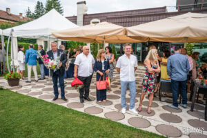 Елегантно облечени гости разговарят и се наслаждават на напитки по време на "welcome drink" преди сватбената церемония във Вила Екатерина. Кадър от сватбен фотограф Симеон Сълов.