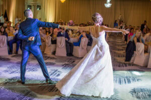 Младоженците Саня и Радослав изпълняват изящна танцова фигура с разперени ръце по време на своя първи сватбен танц в хотел Маринела, кадър на професионален сватбен фотограф Симеон Сълов.