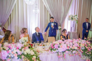 Кумът се обръща с топли думи и усмивка към младоженеца Радослав по време на своята кумова реч на сватбеното тържество в хотел Маринела, кадър на професионален сватбен фотограф Симеон Сълов.