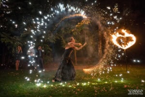 Артист изпълнява зрелищно огнено шоу с искри и пламтящо сърце като изненада на сватбено тържество, динамичен кадър, заснет от сватбен фотограф Симеон Сълов.