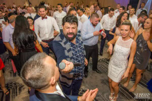 Тони Стораро подава своя микрофон на младоженеца Радослав, за да пее, създавайки уникален момент на голямата им сватба в хотел Маринела, кадър на професионален сватбен фотограф Симеон Сълов.