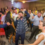 Тони Стораро пее с вдигнат юмрук, докато младоженците Саня и Радослав танцуват до него в препълнената бална зала на хотел Маринела, кадър на професионален сватбен фотограф Симеон Сълов.