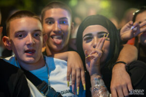 Професионален фотограф заснема отблизо весела компания младежи на Слатина Фест 2025, момиче прави V-знак, а момче се плези.