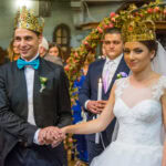 Красив портрет на коронясаните младоженци, хванати за ръце по време на сватбената си церемония в храм „Света Параскева“.