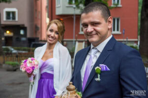 Портрет на кума и кумата, които позират усмихнати пред храм „Света Параскева“ в София по време на сватбения ден.