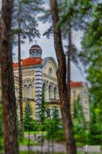 Артистичен кадър на архитектурата на Софийската духовна семинария, заснет през дърветата в парка. Кадър от сватбен фотограф София Симеон Сълов.