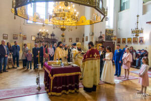 Общ план на църковния брак на Божин и Ханин в храм "Свети Йоан Рилски", който показва младоженците, свещениците и гостите по време на ритуала. Кадър от **сватбен фотограф София** Симеон Сълов.