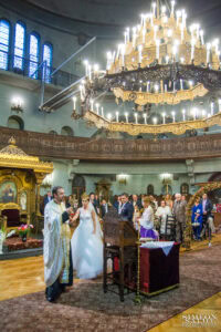 Свещеник води младоженците в „Танцът на Исая“ под големия полилей на храм „Света Параскева“ по време на тяхната венчавка.