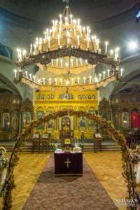 Вертикален кадър на празничната украса за църковен брак в храм „Света Параскева“ в София, показващ олтара и големия полилей.