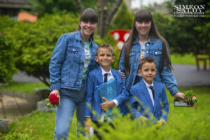 Детски фотограф за дипломиране: Две момчета в сини костюми позират със своите по-големи сестри в зеления двор на детската градина. Кадър от фотограф Симеон Сълов.
