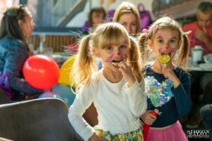 Две момиченца с рисувани муцунки на котета и цветни близалки по време на детски рожден ден на 3 години