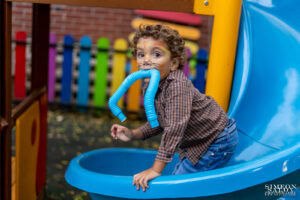 Краси на 3 години с рисувано лице като тигърче играе със синa гъвкава играчка на синя пързалка по време на детски рожден ден