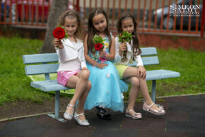 Завършване на детска градина – три момичета с цветя, усмихнати в двора на детската градина, заснети от професионален фотограф в София.