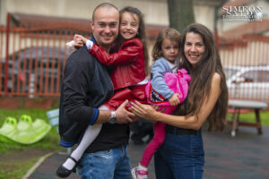 Фотограф за завършване на детска градина: Щастливо семейство позира с дъщеря си, облечена в червен костюм за дипломирането си. Кадър от фотограф Симеон Сълов.