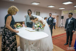 Сватбен фотограф в зала "Оборище": Булката се подписва усмихнато на ритуалната маса за граждански брак, наблюдавана от длъжностното лице. Кадър от Симеон Сълов.