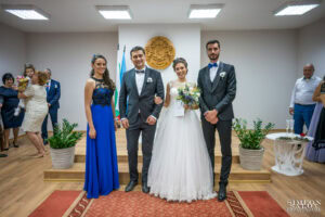 Сватбен фотограф в зала "Оборище": Официална снимка на младоженците и кумовете, позиращи пред герба на София след ритуала по граждански брак. Кадър от Симеон Сълов.