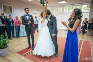 Сватбен фотограф в зала "Оборище": Младоженците се целуват за първи път като семейство, а булката вдига букета си под аплодисментите на кумовете. Кадър от Симеон Сълов.