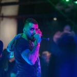 Професионална сценична фотография на Венци Венц (Venci Venc), заснета от Симеон Сълов. Изпълнителят е уловен в близък план, гледащ директно в обектива, докато пее на микрофон под въздействащо синьо и зелено клубно осветление.